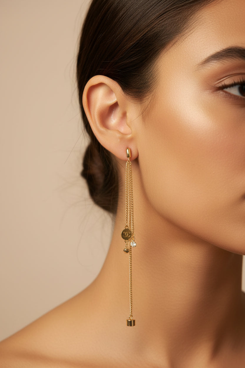 A pair of gold earrings with small dangling charms, displayed on a black textured surface.