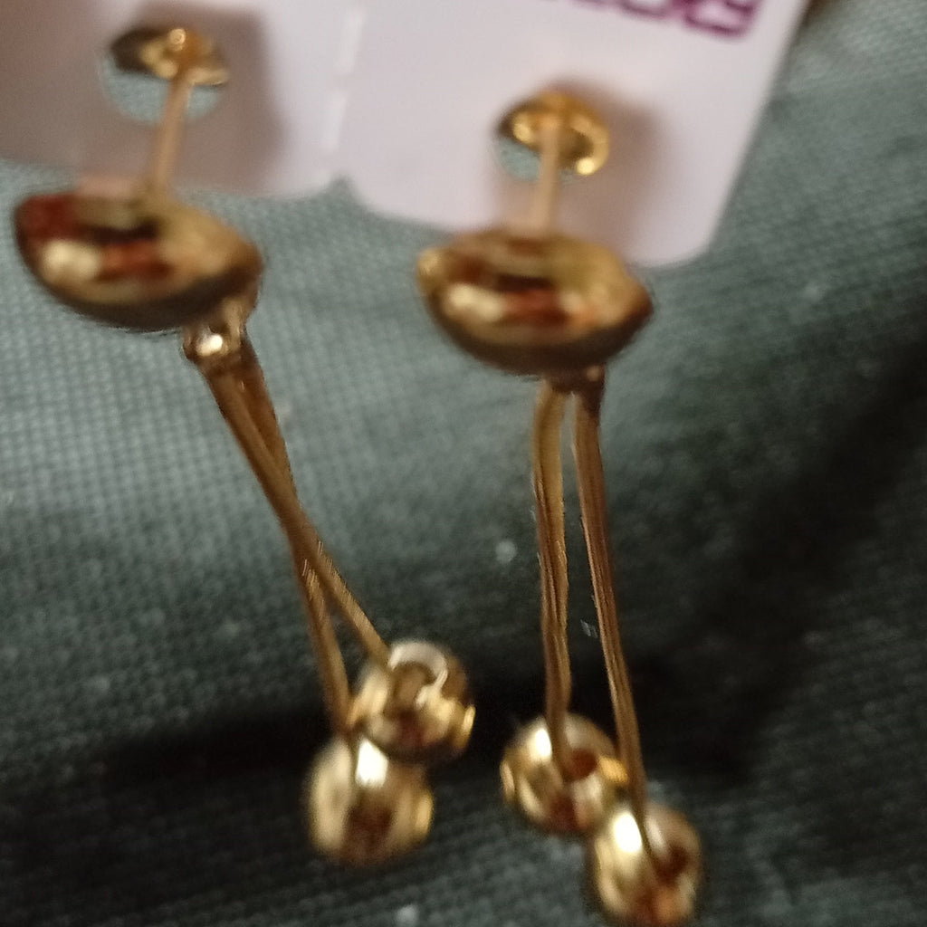 Gold dangling earrings with multiple small bead-like drops, attached to white cards printed with 'FASHION JEWELRY', held near a finger against a dark textured fabric background.