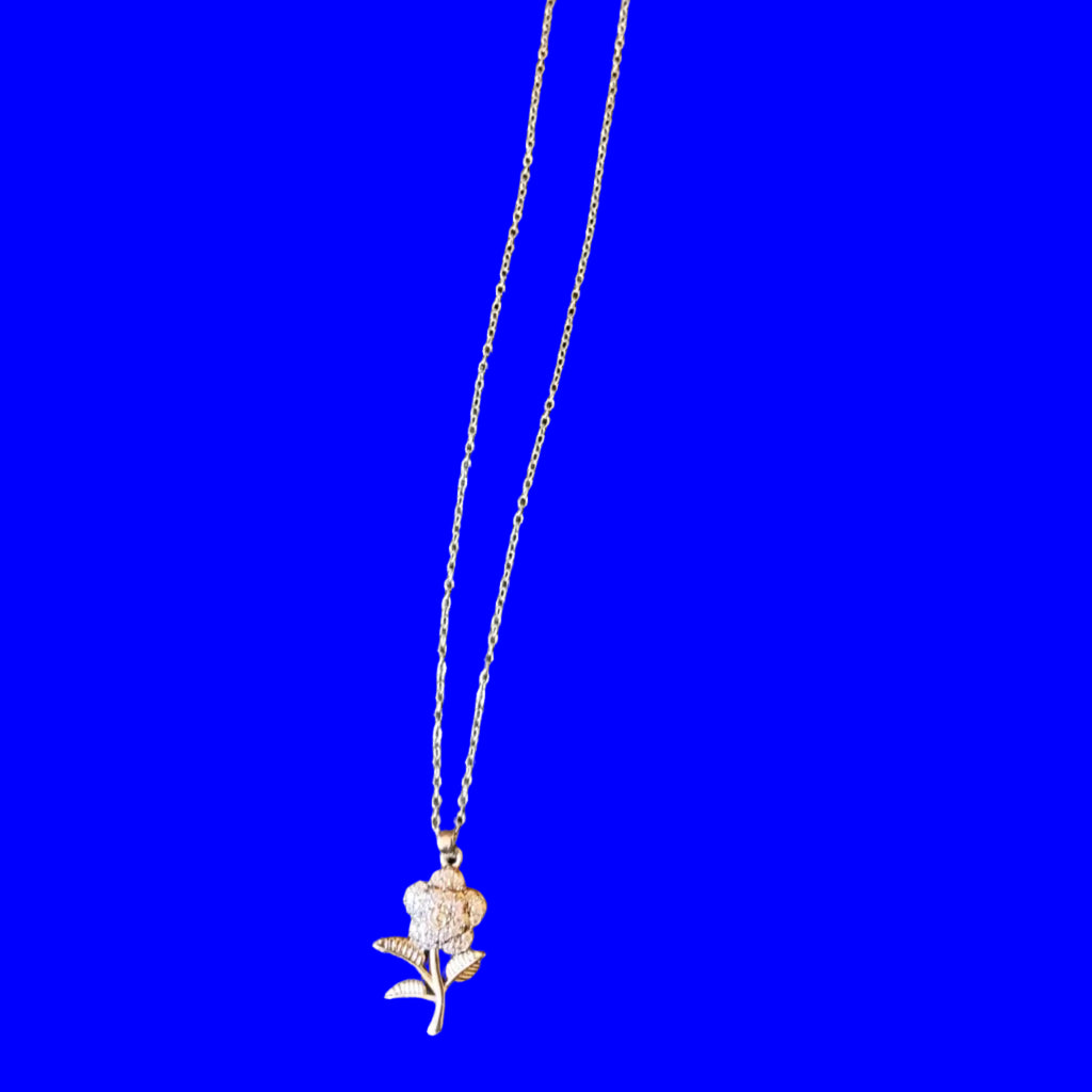 A delicate silver-toned chain necklace with a small rose charm and a white paper hangtag, laid flat on a black textured fabric background.