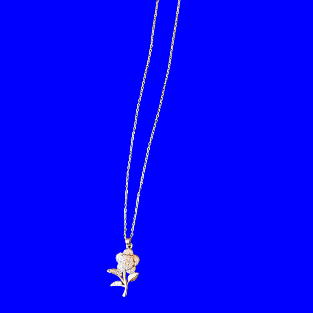 A delicate silver-toned chain necklace with a small rose charm and a white paper hangtag, laid flat on a black textured fabric background.