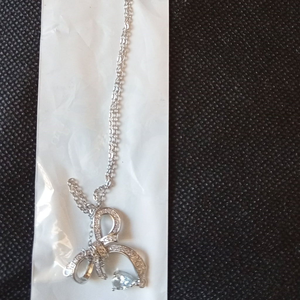Silver stainless steel chain necklace with a bow-shaped pendant and butterfly charm, displayed on its white cardboard packaging against a black textured background.
