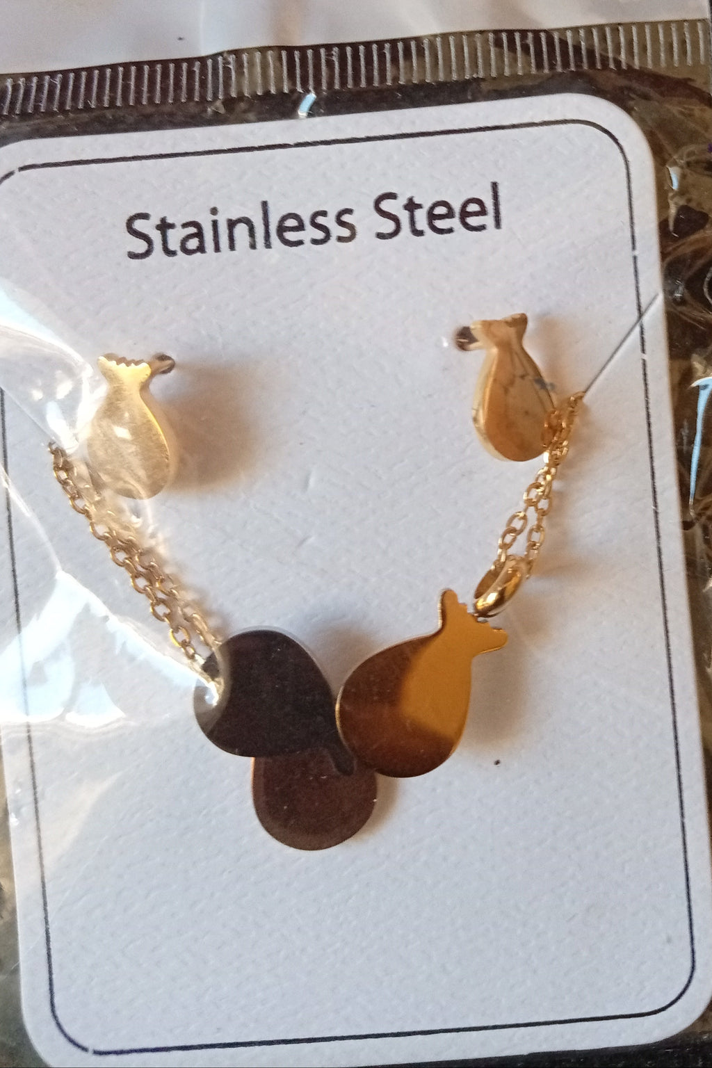 A stainless steel fish charm chain on a white display card inside a clear plastic sleeve, photographed on a dark textured surface.