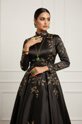 A gold-toned jewelry set with green stones, including a necklace, earrings, and a bracelet, displayed on a white card with a hand holding the bracelet at the bottom against a black textured background.