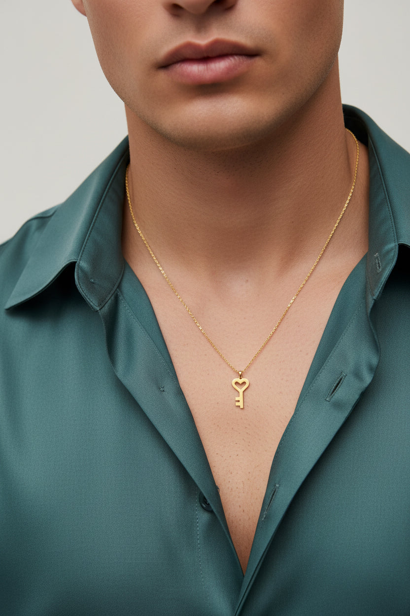 A gold-colored metal key-shaped pendant necklace on a matching chain, displayed on a black textured fabric background.