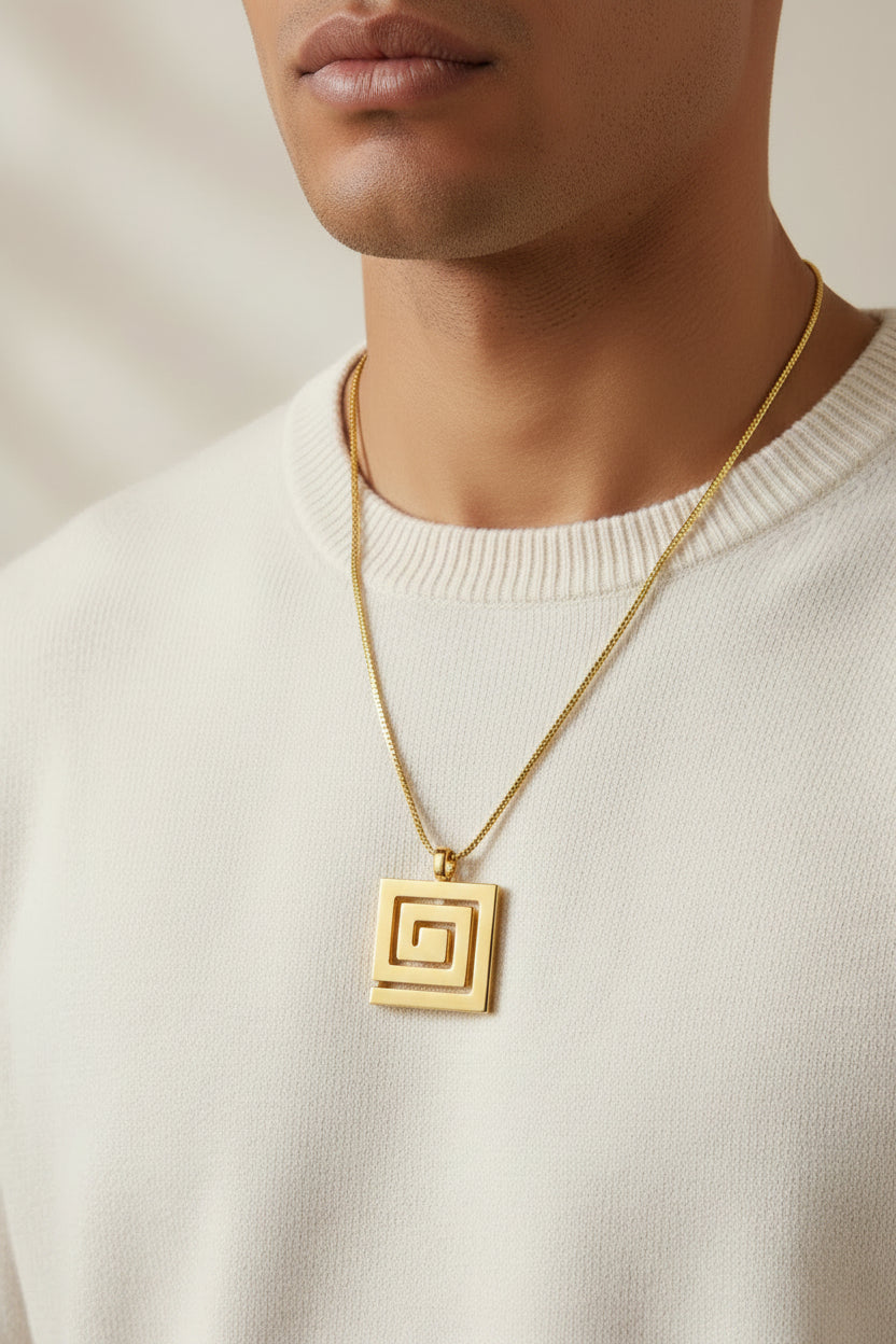 A gold-toned metal chain necklace with a square geometric pendant, laid out on a black textured fabric surface.