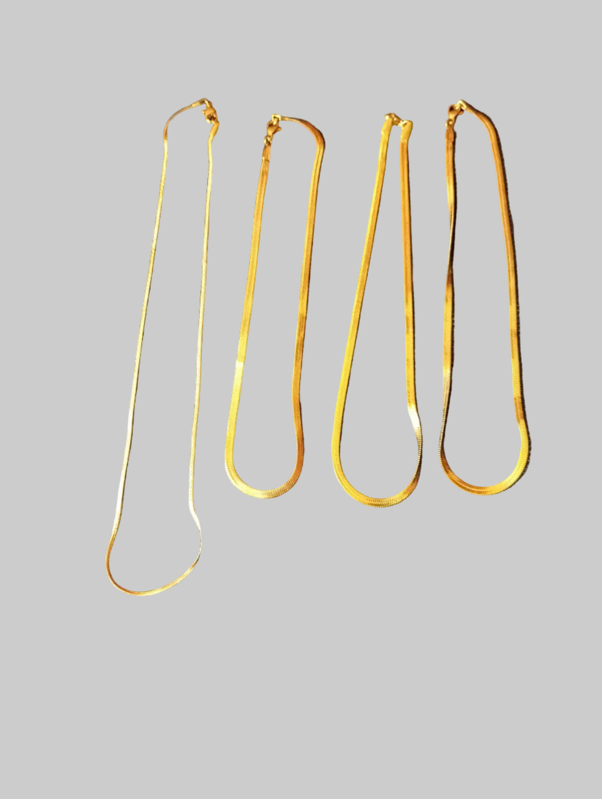 Four gold-colored metal chains laid out on a dark textured fabric background, with some text partially visible on the left edge.